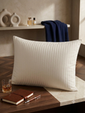 White pillow on a wooden surface with a notebook, glass, and pen in a home setting.